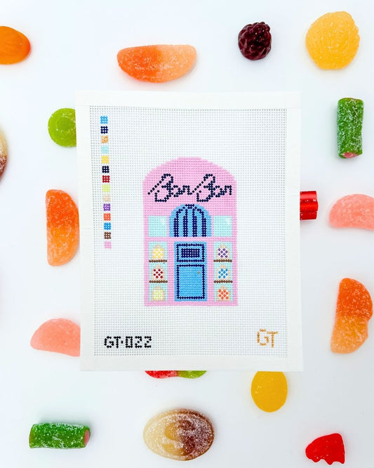 Needlepoint canvas design of a colorful candy shop with 'BonBon' text, surrounded by candy on a white background.